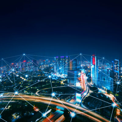 A city skyline at night with illuminated buildings and highways, overlaid with digital network lines and glowing points, symbolizing connectivity and technology integration.