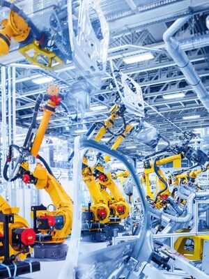 Yellow robotic arms assemble car bodies in a bright, modern factory with metal pipes and overhead lights, illustrating advanced automation in automotive manufacturing.