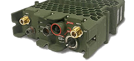A close-up of a rugged, olive-green military radio communication device with multiple ports and connectors, including gold and black circular sockets, and a honeycomb-patterned top surface.