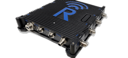 A black electronic device with multiple connection ports on its side, ribbed casing, and a large blue logo featuring the letter "R" with a wireless signal symbol on top.