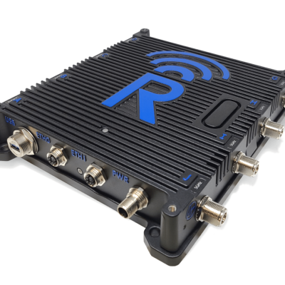 A black electronic device with ribbed casing, blue accents, multiple input/output connectors, and a large blue "R" logo with wireless signal lines on the top. The connectors are labeled SIM, ETH1, BTC1, BWA, and AUX.