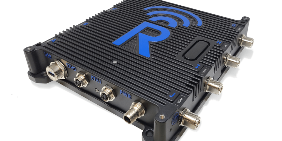 A black electronic device with ribbed casing, blue accents, multiple input/output connectors, and a large blue "R" logo with wireless signal lines on the top. The connectors are labeled SIM, ETH1, BTC1, BWA, and AUX.