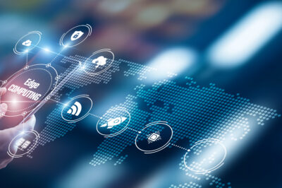 A person’s hand interacts with a transparent touchscreen displaying digital icons and the words “Edge Computing,” with a stylized world map and glowing network connections in the background.