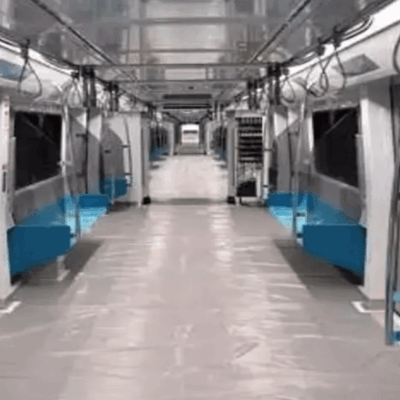 Interior of an empty modern metro train carriage with blue seats along both sides, handrails above, and large windows. The floor is clean and reflective, and the carriage appears well-lit and spacious.