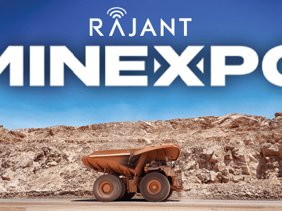 A large mining dump truck sits in front of a rocky landscape under a blue sky, with "Rajant MINEXPO" written in bold white letters across the top of the image.
