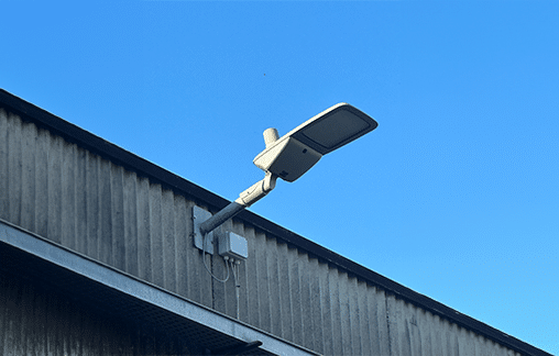A modern streetlight attached to the side of a corrugated metal building, set against a clear blue sky.