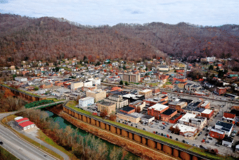 Aerial view of a small town with brick buildings, houses, and roads, surrounded by forested hills with bare trees and a river running alongside the town.
