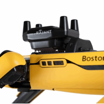 Close-up view of a yellow Boston Dynamics robot with a black Rajant wireless device mounted on top, showing robotic joints and part of the Boston Dynamics logo.