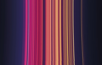 Vertical streaks of vibrant colors, including shades of pink, red, orange, and yellow, blend and flow against a dark purple background, creating an abstract, luminous effect.