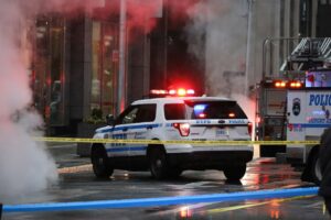 A New York Police Department SUV with flashing lights is parked behind yellow police tape on a city street, surrounded by steam and emergency vehicles.