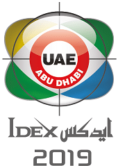 IDEX 2019 logo featuring a circular design with "UAE ABU DHABI" in the center, surrounded by green, yellow, blue, and gray segments, with crosshairs overlaid, and "IDEX 2019" in English and Arabic below.