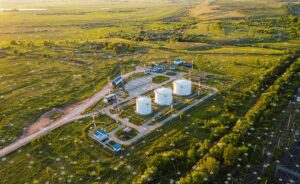 Aerial view of a rural industrial facility with large white storage tanks, surrounded by green fields, buildings, and roads, with digital network graphics overlaid on the image.