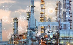 An industrial refinery with tall structures and pipes is overlaid with digital network icons and lines, symbolizing connections, data, and industrial technology integration. Sky is cloudy in the background.