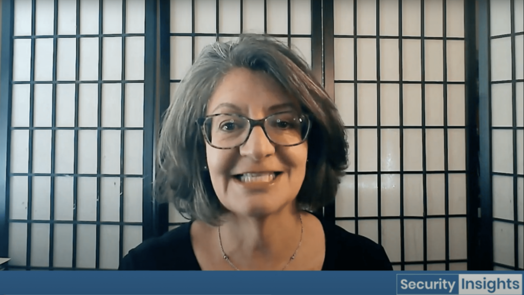 A woman with glasses and shoulder-length gray hair smiles at the camera, sitting in front of a folding screen. The words "Security Insights" appear in the lower right corner of the image.