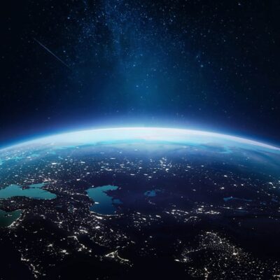 View of Earth from space showing a curved horizon, illuminated landmasses, bright city lights, and a star-filled night sky above.