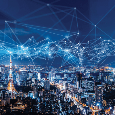 A city skyline at night is overlaid with glowing, interconnected lines and nodes, symbolizing digital connectivity, data networks, or communication technology. Tall buildings and bright city lights are visible below the network overlay.