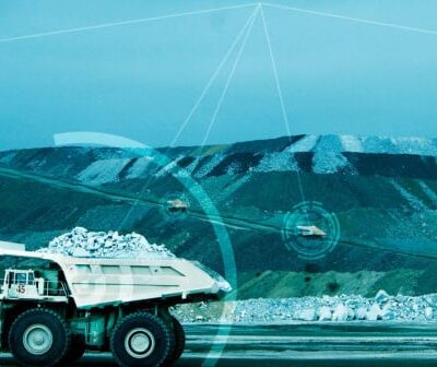 A large mining dump truck filled with rocks drives through a quarry, with digital graphics overlaying the image, suggesting advanced technology or automation in the mining process.