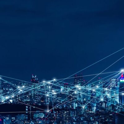 A city skyline at night with illuminated buildings and white lines connecting points across the sky, representing a digital network or smart city technology.