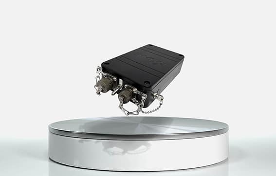 A small black electronic device with metal connectors is suspended above a round, white display platform against a plain light background.