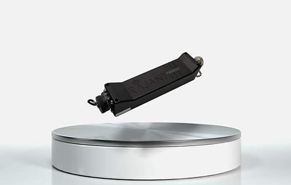 A small black electronic device is shown levitating above a round, metallic, and white platform against a plain light background.