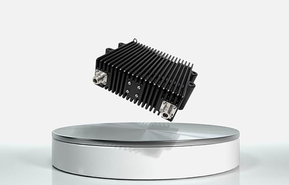 A black, rectangular electronic device with cooling fins is suspended above a round, white pedestal against a plain white background.