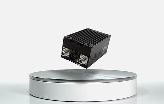 A black electronic device with cooling fins and multiple ports is floating above a round, silver and white pedestal against a plain white background.