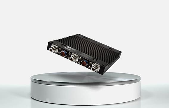 A black, rectangular electronic device with multiple connectors on one side is displayed hovering above a round, white platform against a plain, light background.