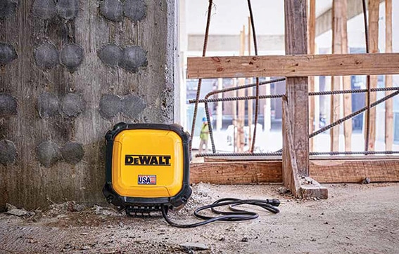 A yellow DEWALT portable power station with a black cord is placed on a dusty concrete floor at a construction site, near a marked concrete wall and wooden framing.