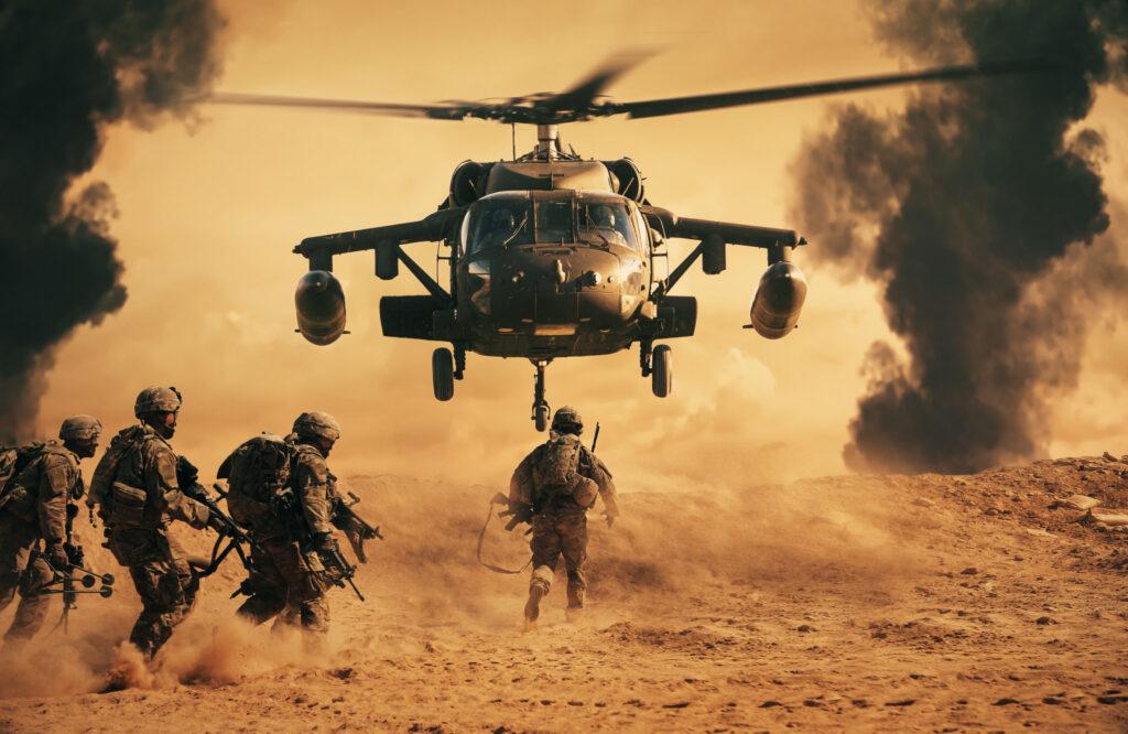 A military helicopter hovers above sandy terrain as soldiers in combat gear run toward it. Smoke and dust fill the air, creating a tense, dramatic scene with a sunset-colored sky in the background.