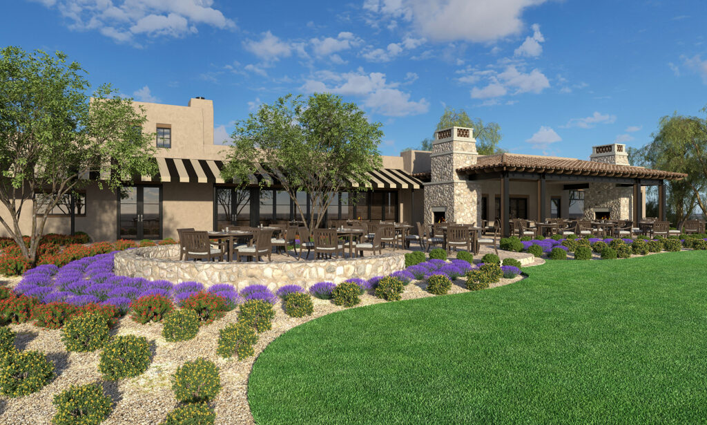 Outdoor patio area with wooden tables and chairs, surrounded by stone landscaping, colorful flowers, and green lawn. The building has stone walls, large windows, striped awnings, and a covered fireplace area under a wooden pergola.