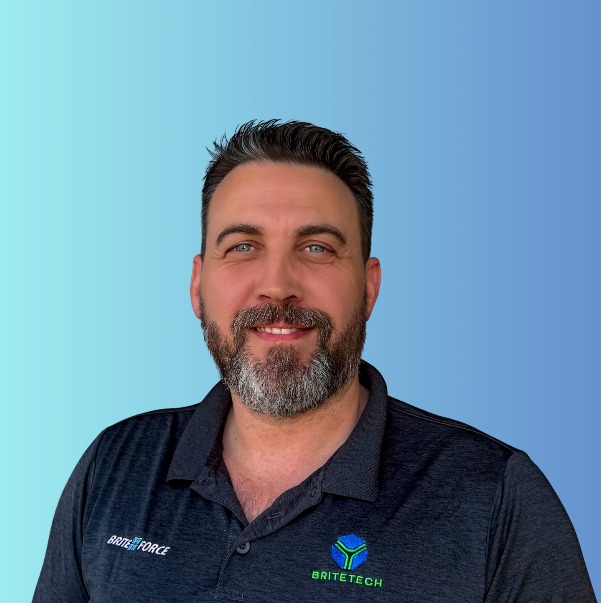 A man with short dark hair and a beard, wearing a black collared shirt with “BRITE FORCE” and “BRITE TECH” logos, smiling in front of a blue gradient background.